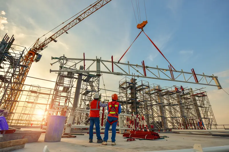 Workers guiding a steel truss lowered by a tower crane over a scaffolded structure