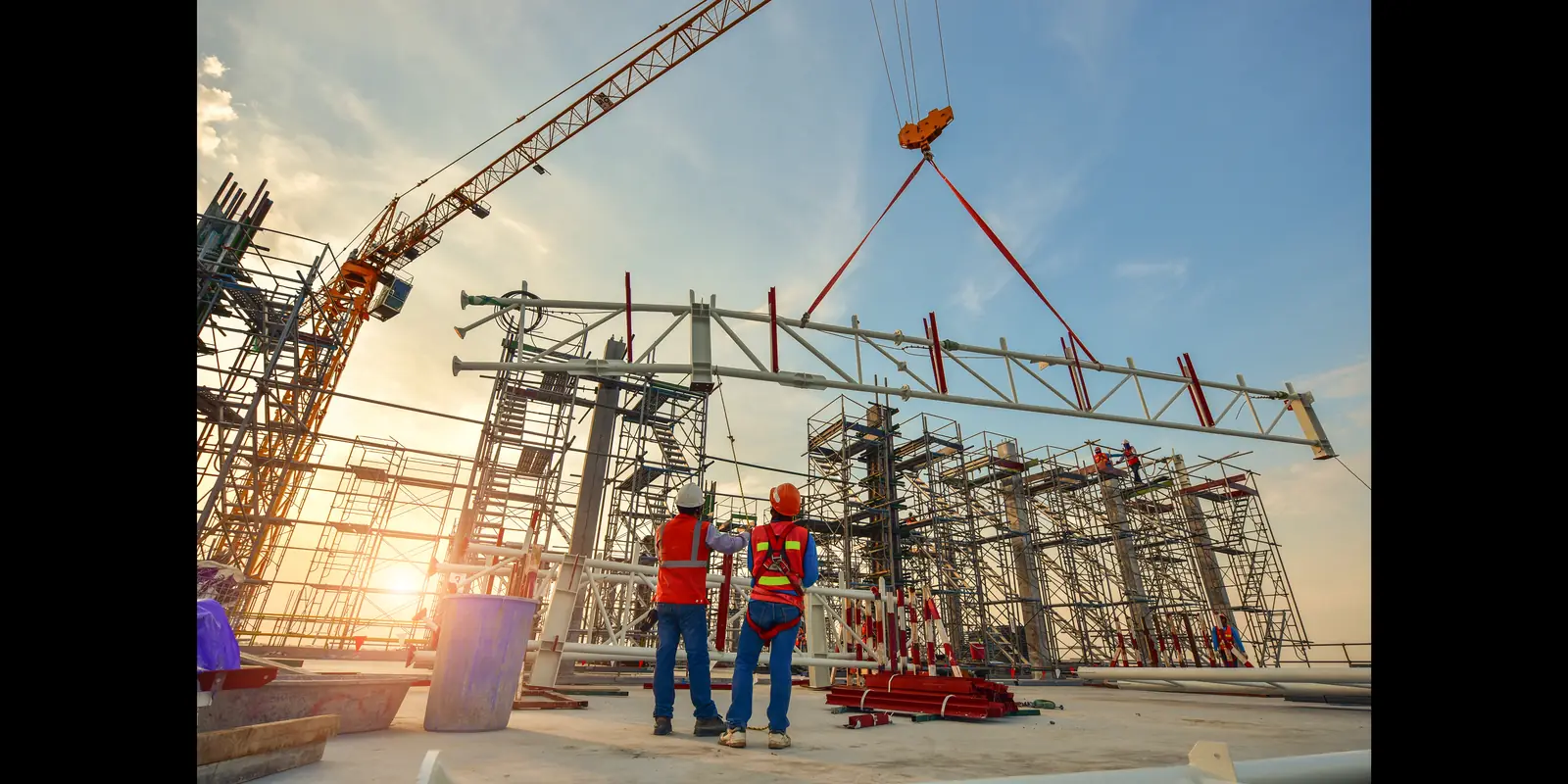 Workers guiding a steel truss lowered by a tower crane over a scaffolded structure