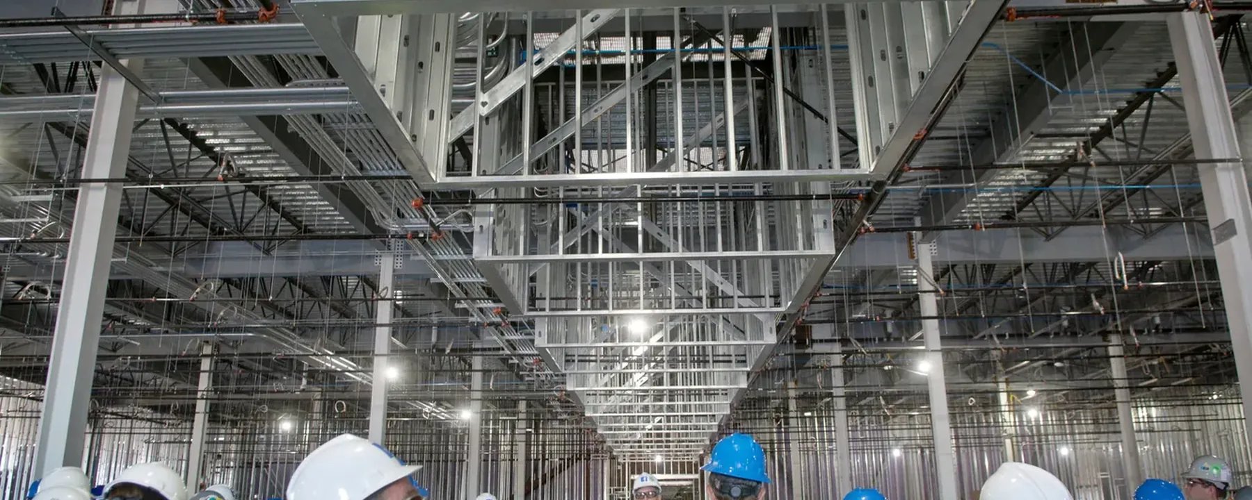 Group in hard hats and high-visibility vests walking a plant room lined with overhead ductwork and cable tray