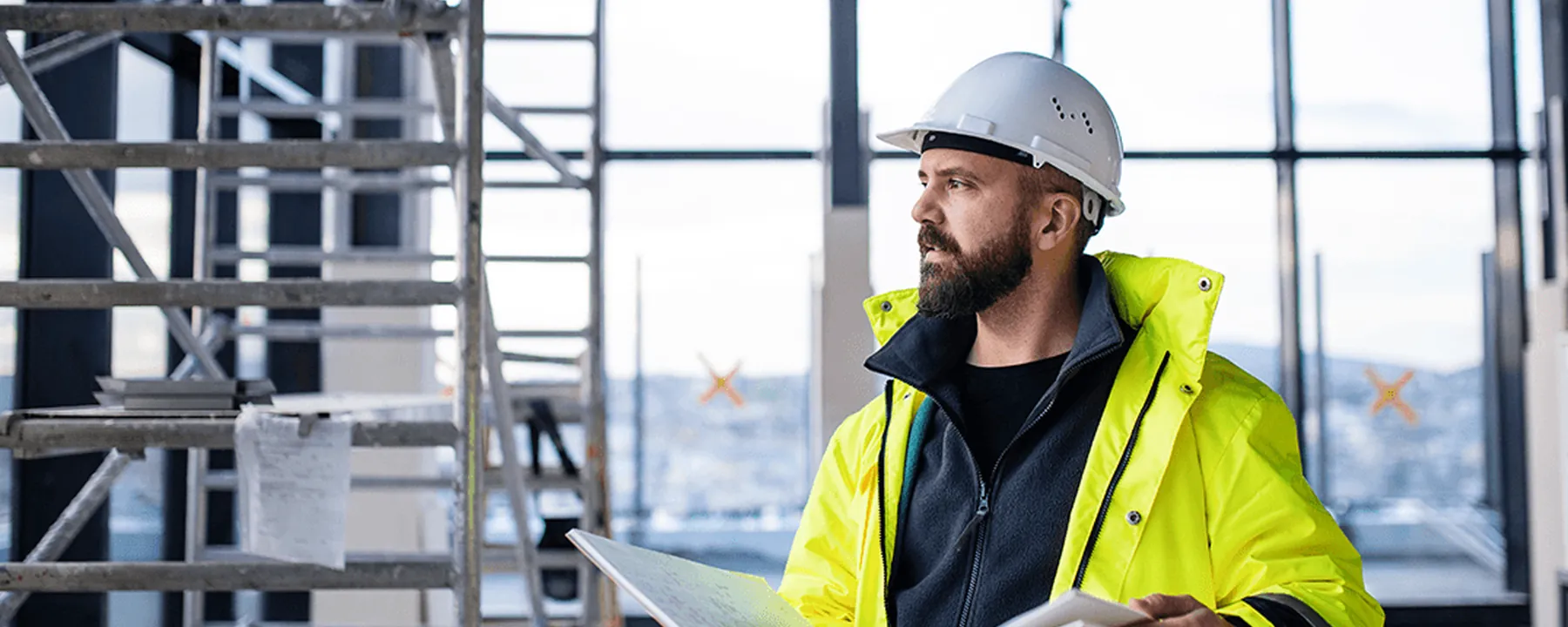 Project manager in a high-visibility jacket and hard hat reading an open document folder inside a glazed building under fit-out