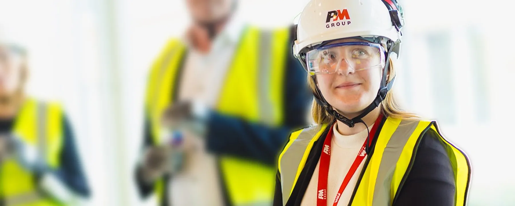 Site engineer in a hard hat and safety glasses on a project walk, a colleague out of focus behind her