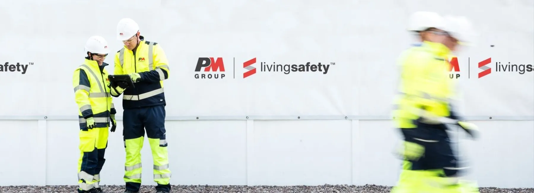 Workers in high-visibility gear walking along a site hoarding on a live construction project